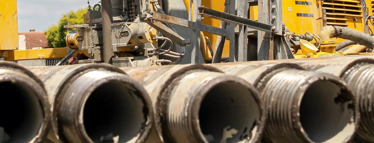 Foto zeigt im Vordergrund Metallrohre, im Hintergrund ein gelbes Bohrgerät