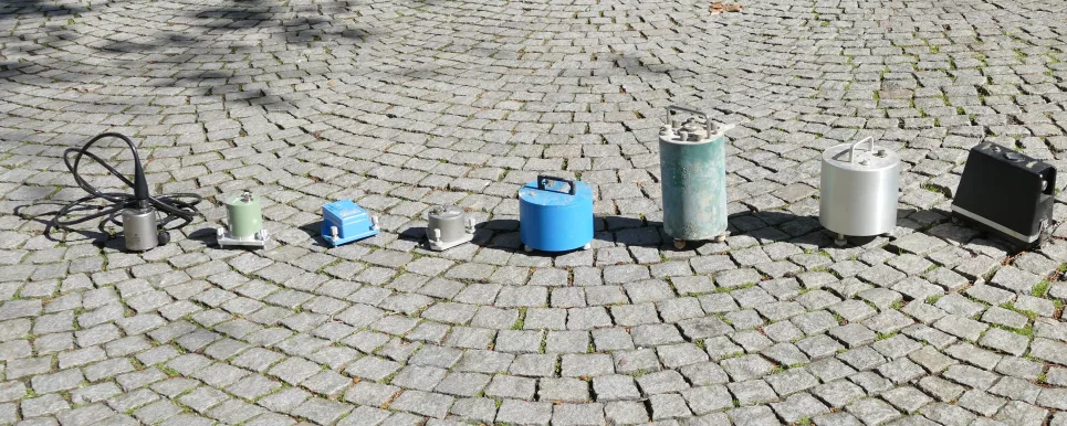 Auf Kopfsteinpflaster stehen in einer Reihe verschiedene Seismometertypen, also Geräte zum Messen von Erdbebensignalen
